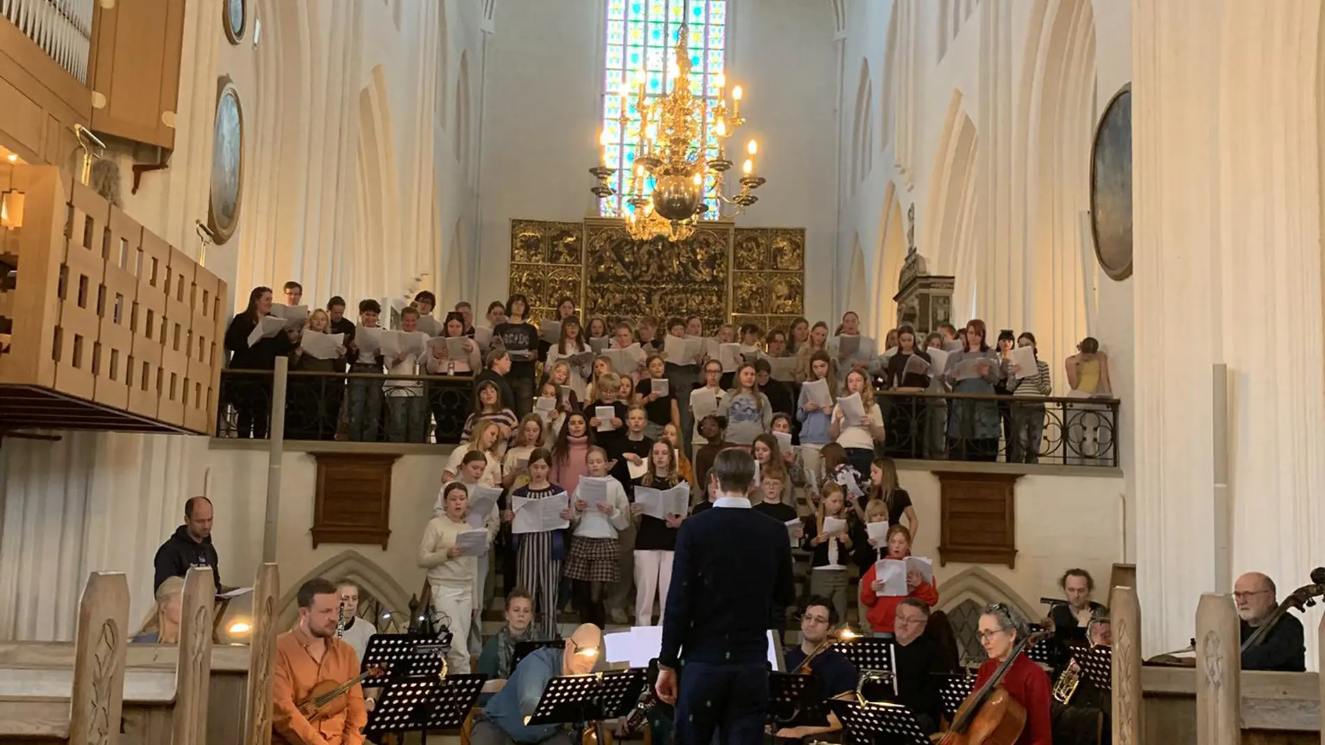 Et børnekor og et orkester øver fremvisning i en kirke