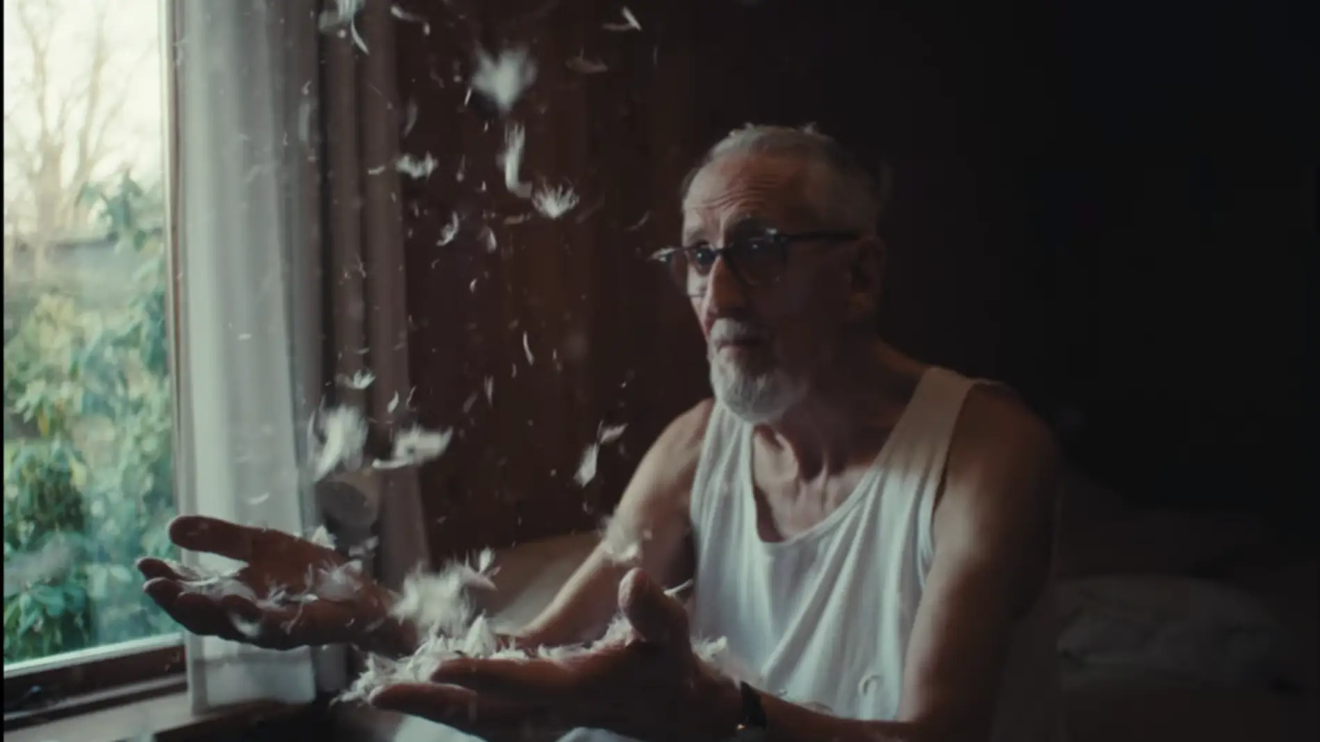 Ældre mand sidder ved vinduet og kaster med hvide dynfjer